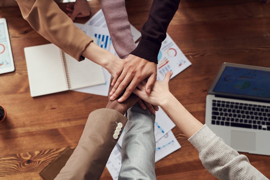 Diverse professionals unite for teamwork around a wooden table with laptops and documents